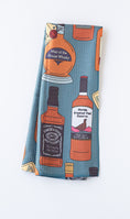Load image into Gallery viewer, A folded towel, featuring a blue-green background with a pattern of illustrated whiskey bottles and labels in orange, black, white, and yellow.