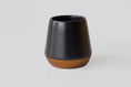 Load image into Gallery viewer, A modern tapered insulated Joey Mug with a matte black upper body and a metallic bronze base, photographed on a clean light gray background.