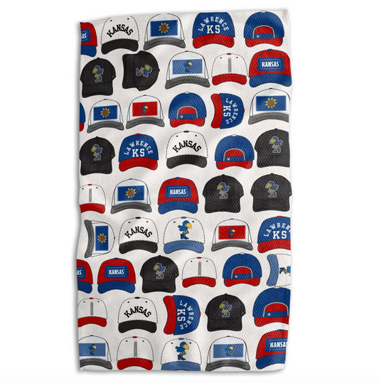 A white towel featuring a repeating pattern of various Kansas Jayhawks-themed snapback hats in blue, red, black, and white.