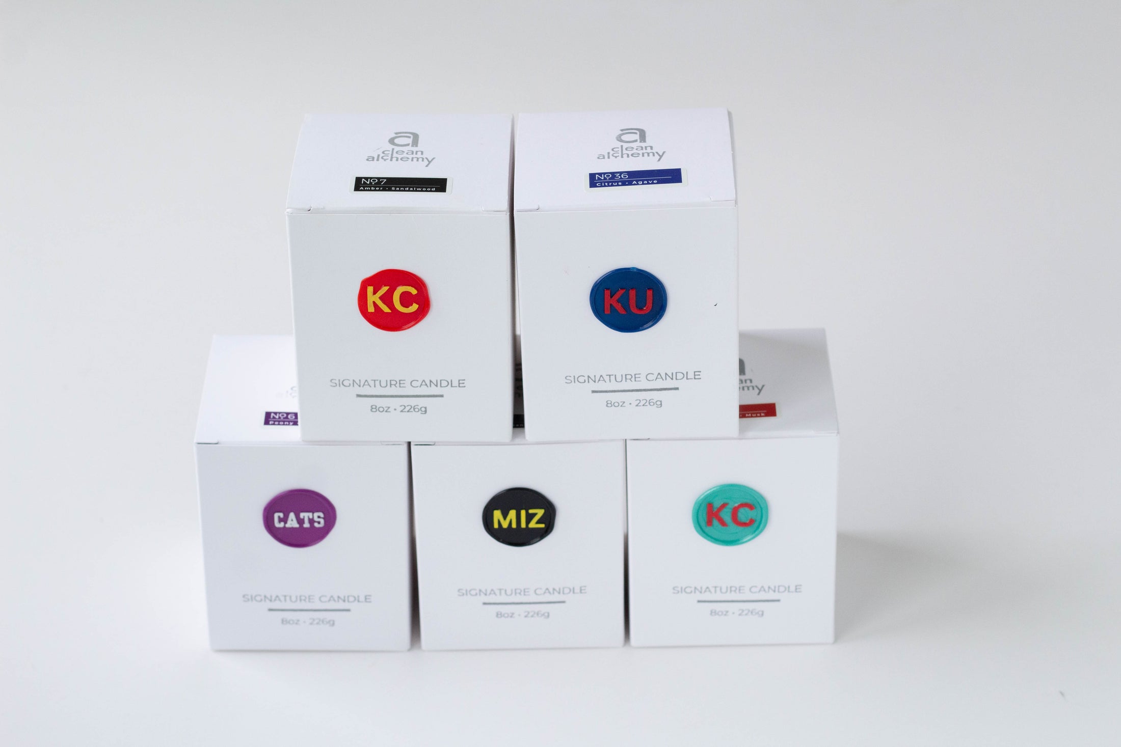 A collection of Kansas City sport & collegiate logos on wax seals on the outside of candle packaging in a variety of scents & fragrances