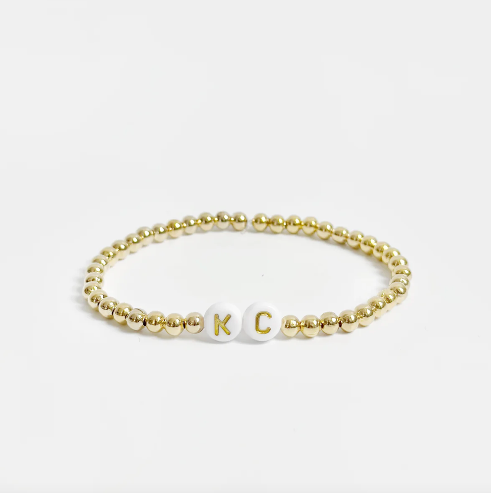 Gold beaded friendship bracelet with white and gold letter beads spelling out "KC" 