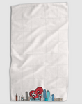 Load image into Gallery viewer, A white textured kitchen towel with a grid pattern, featuring a colorful Kansas City skyline graphic and a red heart with 'KC' in white at the bottom, shown against a light gray background.
