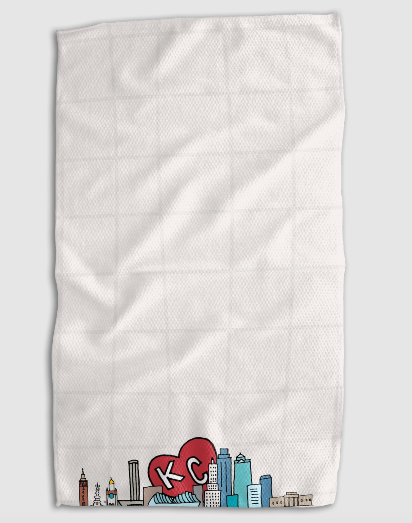 A white textured kitchen towel with a grid pattern, featuring a colorful Kansas City skyline graphic and a red heart with 'KC' in white at the bottom, shown against a light gray background.