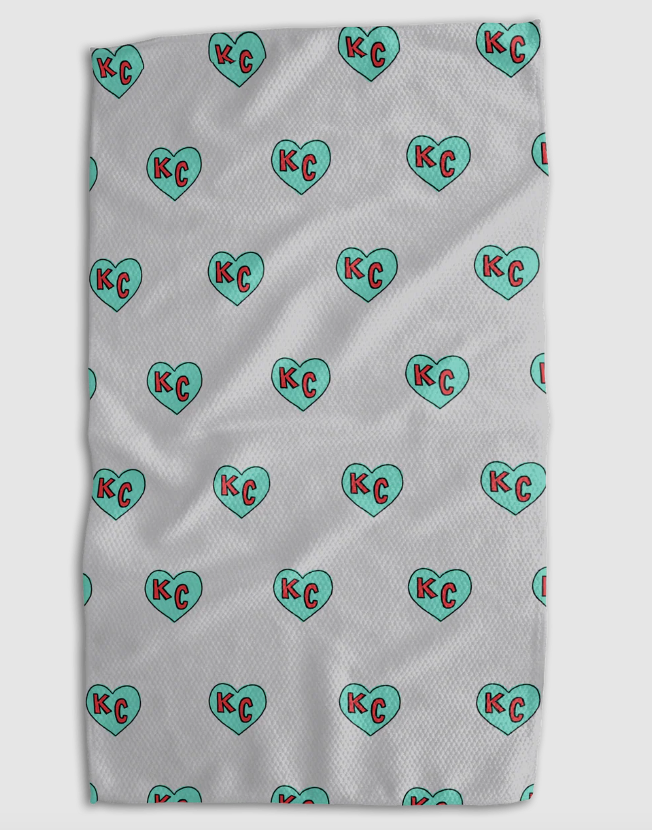 A white textured blanket featuring a repeating pattern of mint green hearts with red 'KC' initials inside, shown flat against a light gray background.