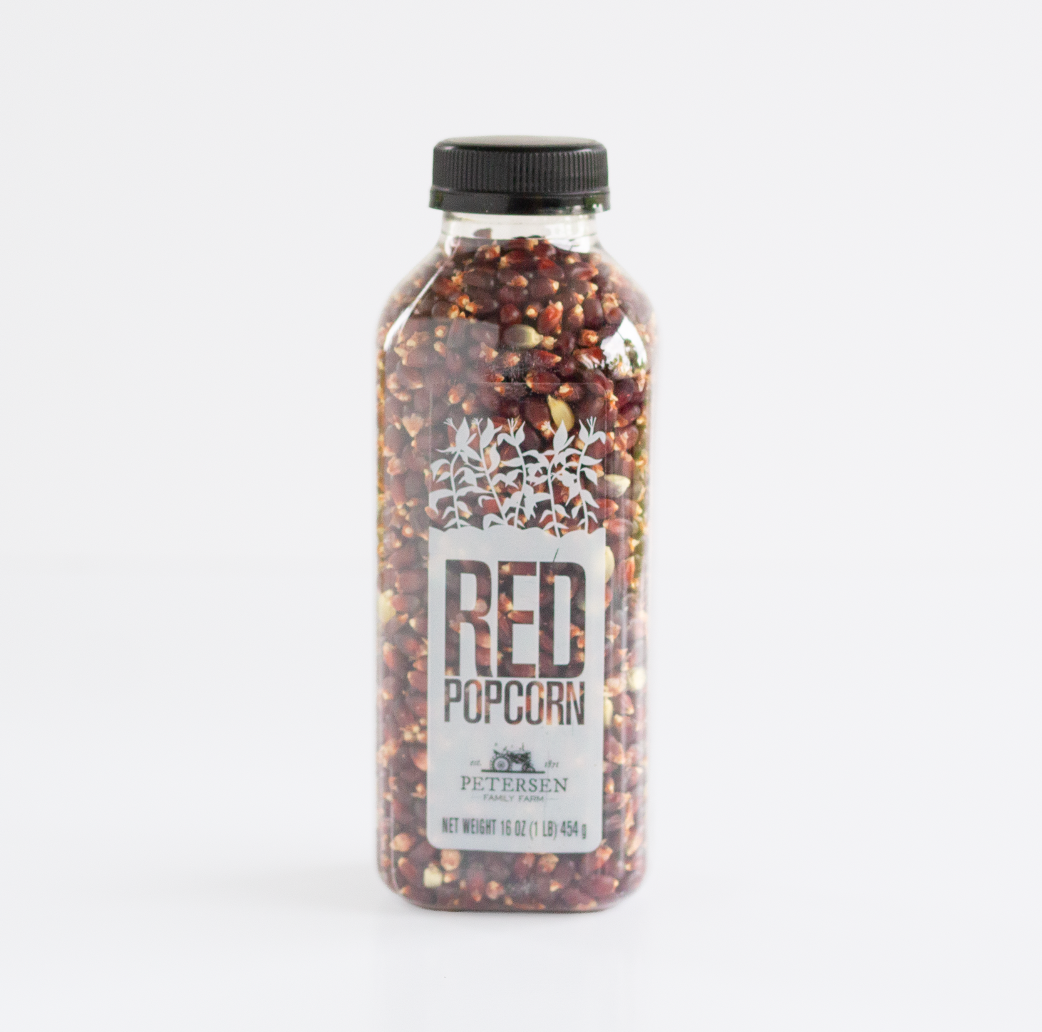 A clear plastic bottle filled with red popcorn kernels, sealed with a black cap, and labeled 'RED POPCORN' with 'Petersen' visible on the front, photographed on a clean white background.