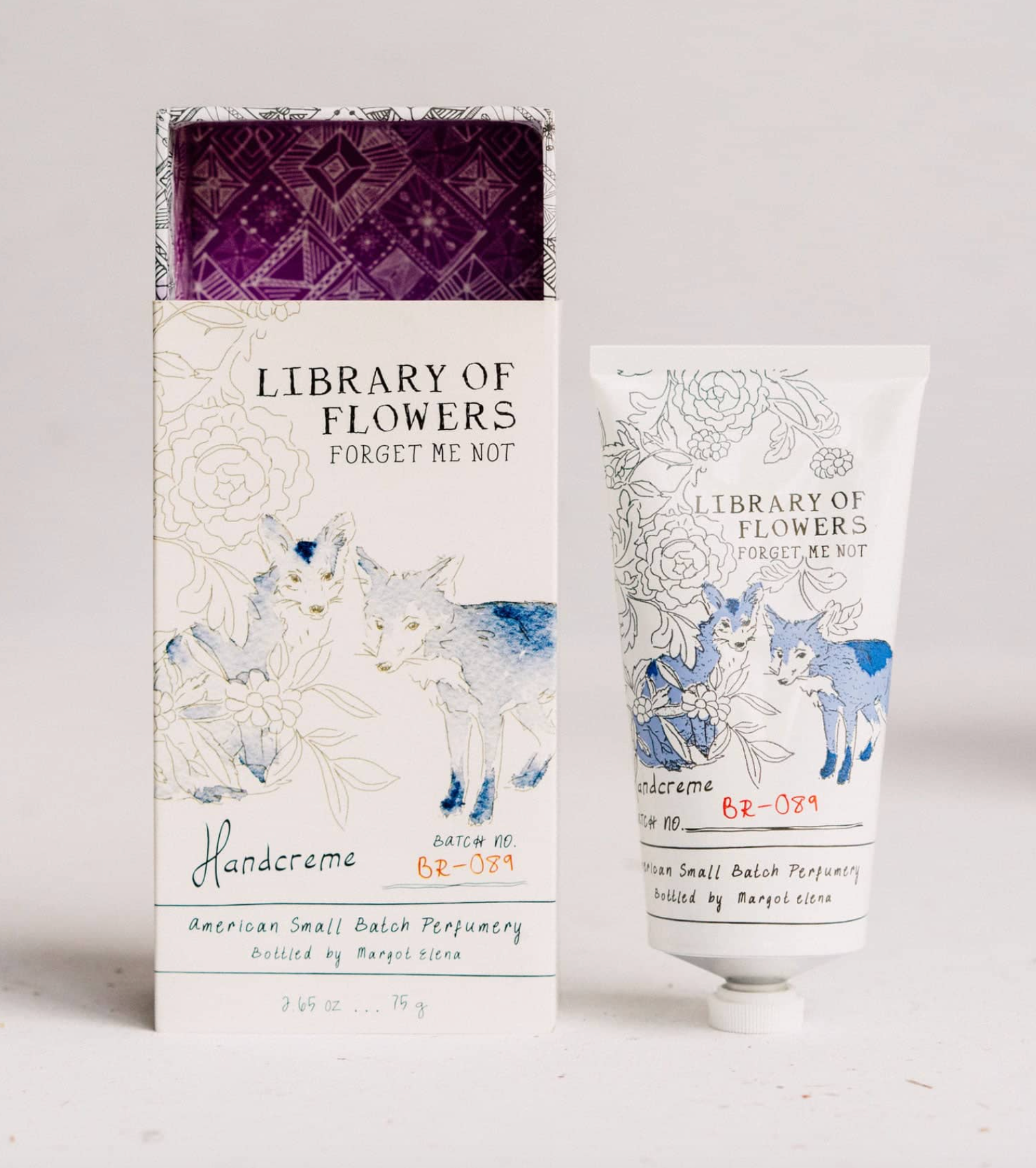 Library of Flowers Forget Me Not Handcreme set, featuring a white box with blue watercolor deer, a white squeeze tube with blue deer illustration, and a purple patterned inner lid, displayed on a white background.