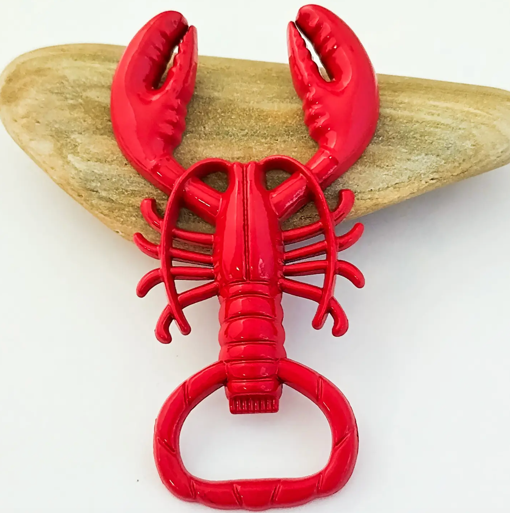 A bright red lobster-shaped bottle opener displayed on a light tan stone against a white background.