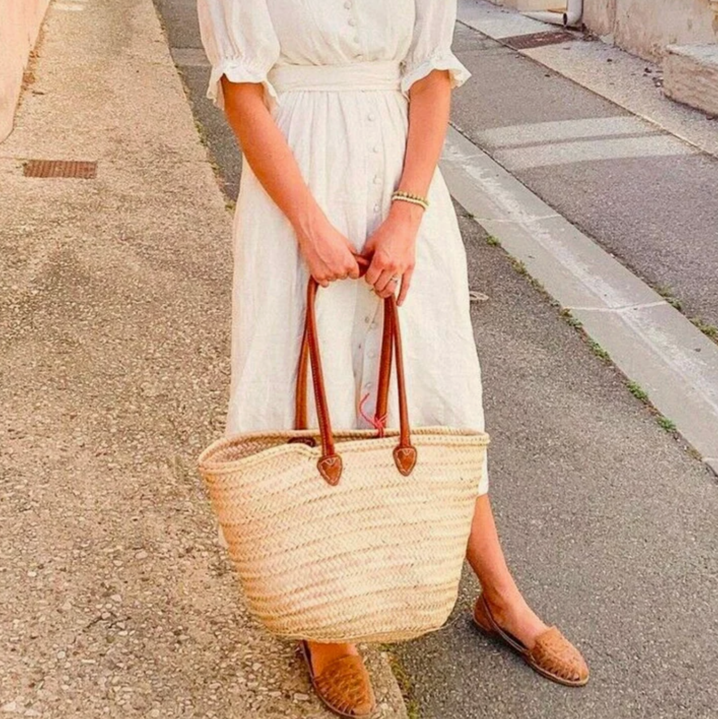 a woman in a long white dress holds a woven market tote with long leather straps