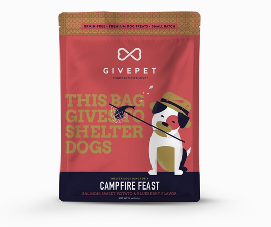 A stand-up pouch of GivePet Campfire Feast dog treats on a plain white background. The package is primarily red with a dark navy band at the bottom, gold text reading 'THIS BAG GIVES TO SHELTER DOGS,' and an illustration of a white dog wearing a hat and holding a treat net.