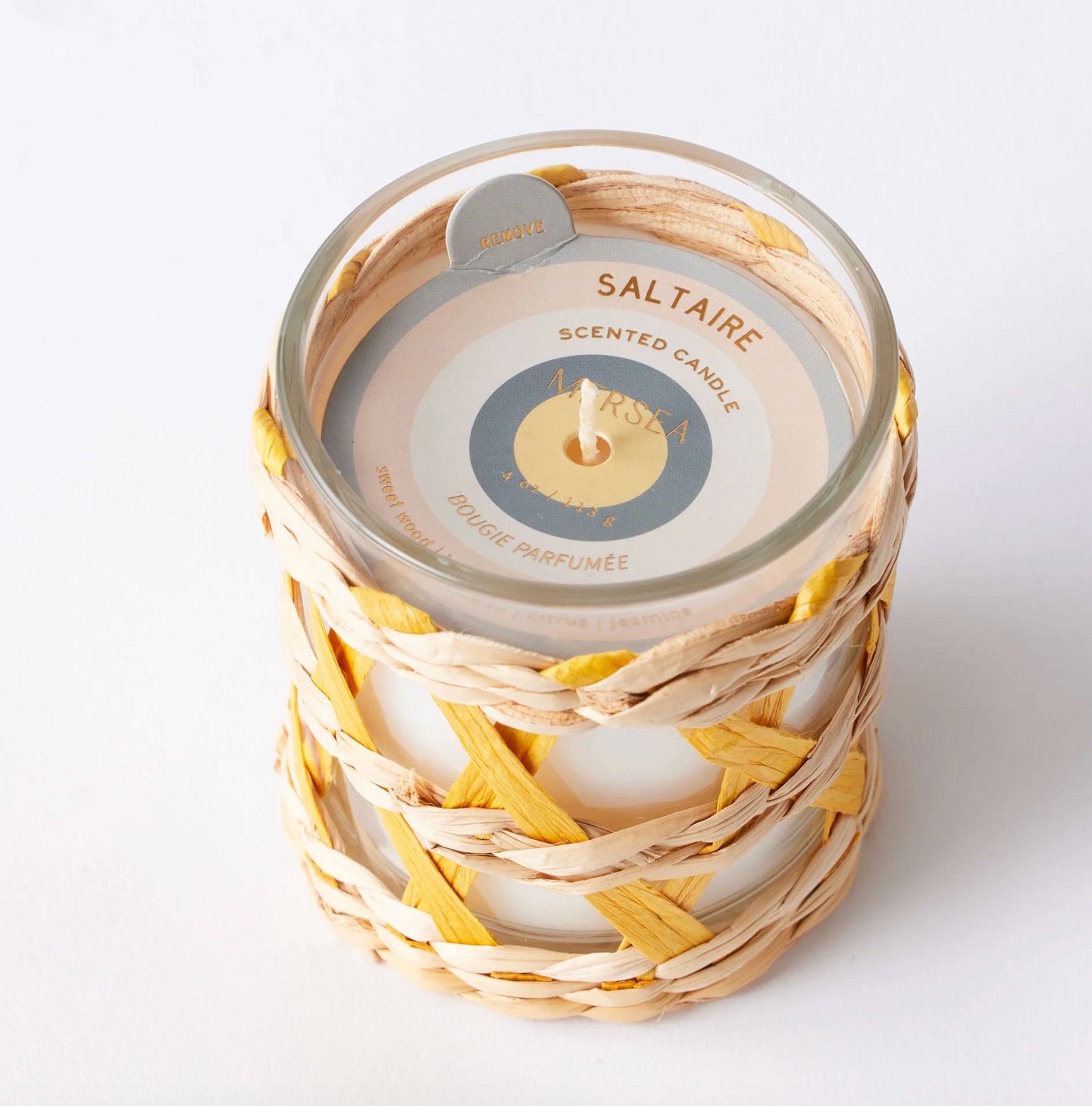 A scented candle in a clear glass jar wrapped in a woven natural fiber sleeve with yellow accents. The top label reads 'SALTAIRE SCENTED CANDLE'.
