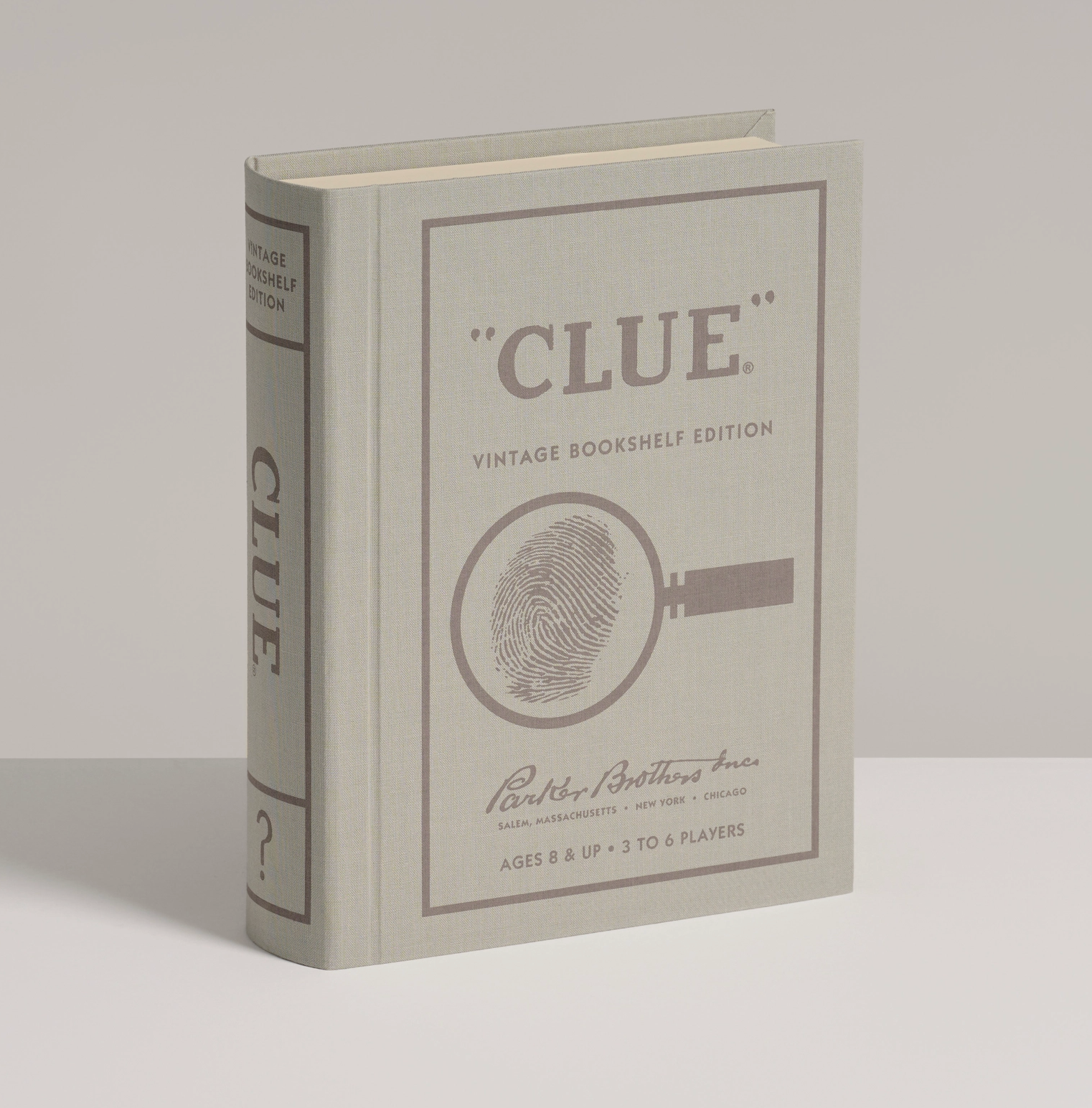A vintage-style bookshelf edition of the board game Clue, shown standing upright on a neutral light gray background. The book features a gray cover with brown printed text and a magnifying glass fingerprint graphic.