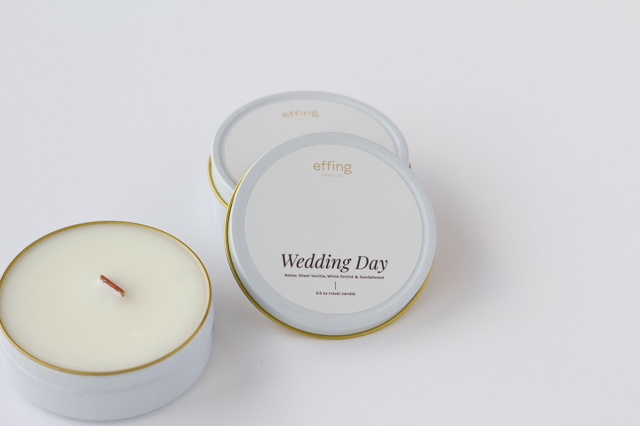 Two round tin candles on a clean white background, including one open candle showing the wax and wood wick, and one closed lids with the label 'Wedding Day' and brand 'effing candle co'.