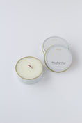 Load image into Gallery viewer, Two round candles in white metal tins with gold rims on a clean white background. One tin is open, showing pale cream wax and a single wood wick, while the other one is closed with white labels reading 'effing candle co' and 'Wedding Day'.
